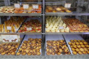 Glass display case filled with assorted pastries, including custard tarts, fruit tarts, and meringue desserts, each labeled with a sign.